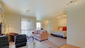 A modern hotel room with a glass dining table, a sofa, a bed, and a large window with blinds. - Aloft Boutique Accommodation (Strahan)