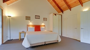 A bedroom with a large bed, a bedside table, a floor lamp, and a door. - Aloft Boutique Accommodation (Strahan)