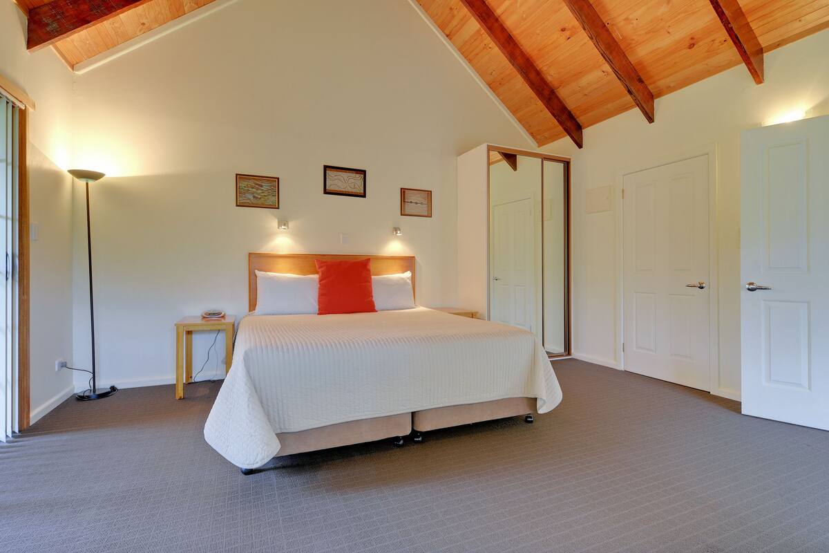 A bedroom with a large bed, a bedside table, a floor lamp, and a door.