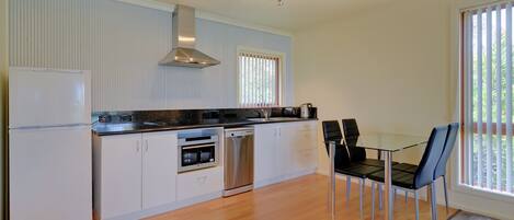 A modern kitchen with white cabinetry, stainless steel appliances, and a dining area with a glass table and chairs.