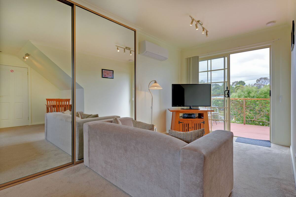 A modern living room with a large flat-screen TV, a sofa, and a dining area with a table and chairs.