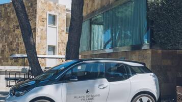 A white electric vehicle parked in front of a building with a stone facade and large windows.