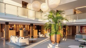 Een ruime lobby met een receptiebalie, zithoeken en een grote potplant.