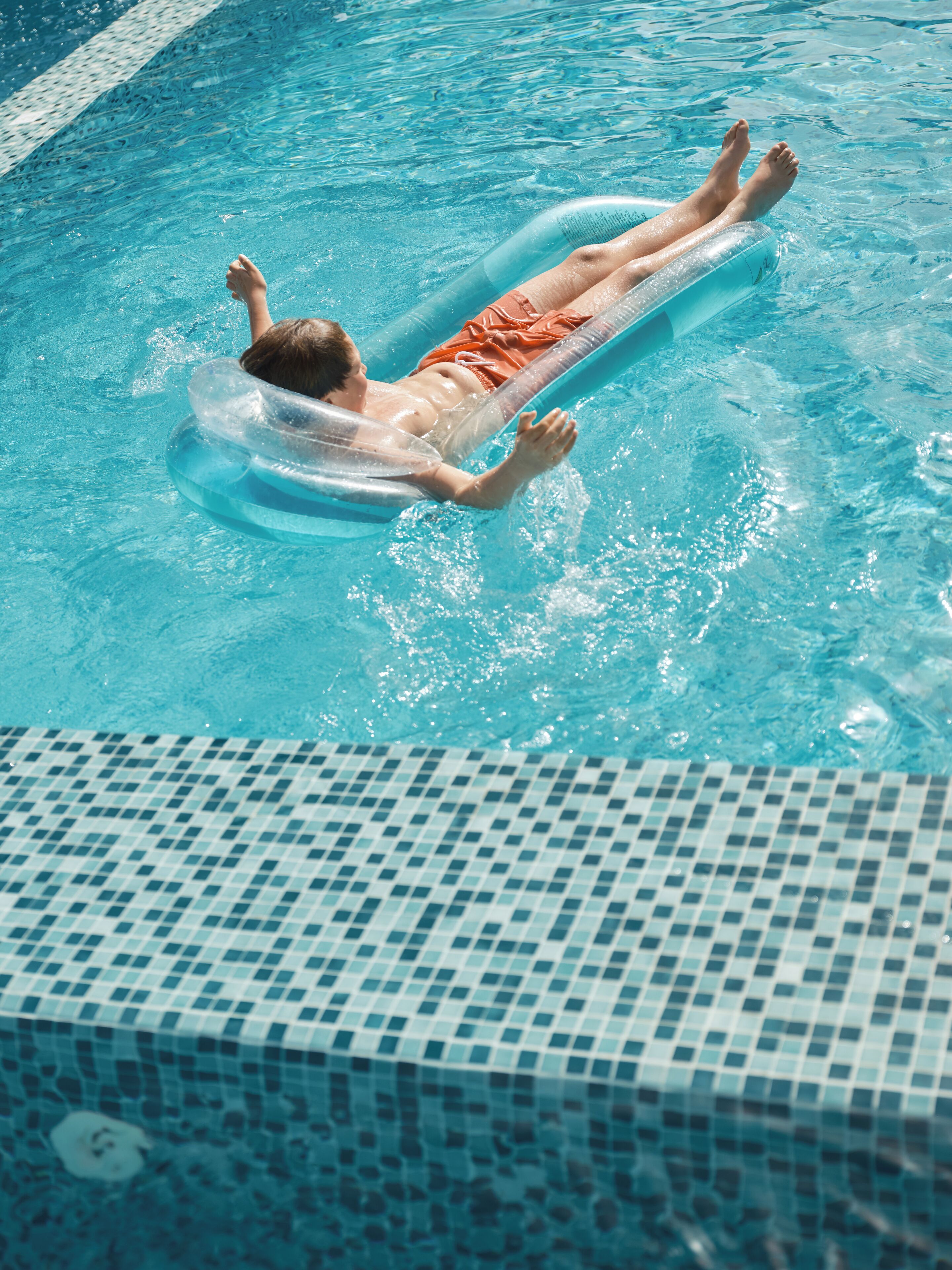 A person floating on an inflatable pool float in a clear blue pool with a tiled edge.