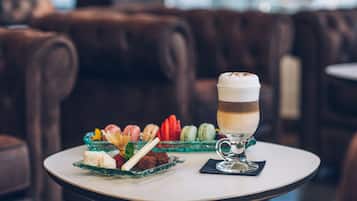 A dessert table with macarons, strawberries, and a layered drink on a white table in a cozy setting with brown leather seating.