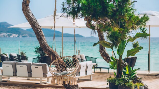 Een strandlounge met een hangstoel, witte banken en potplanten.