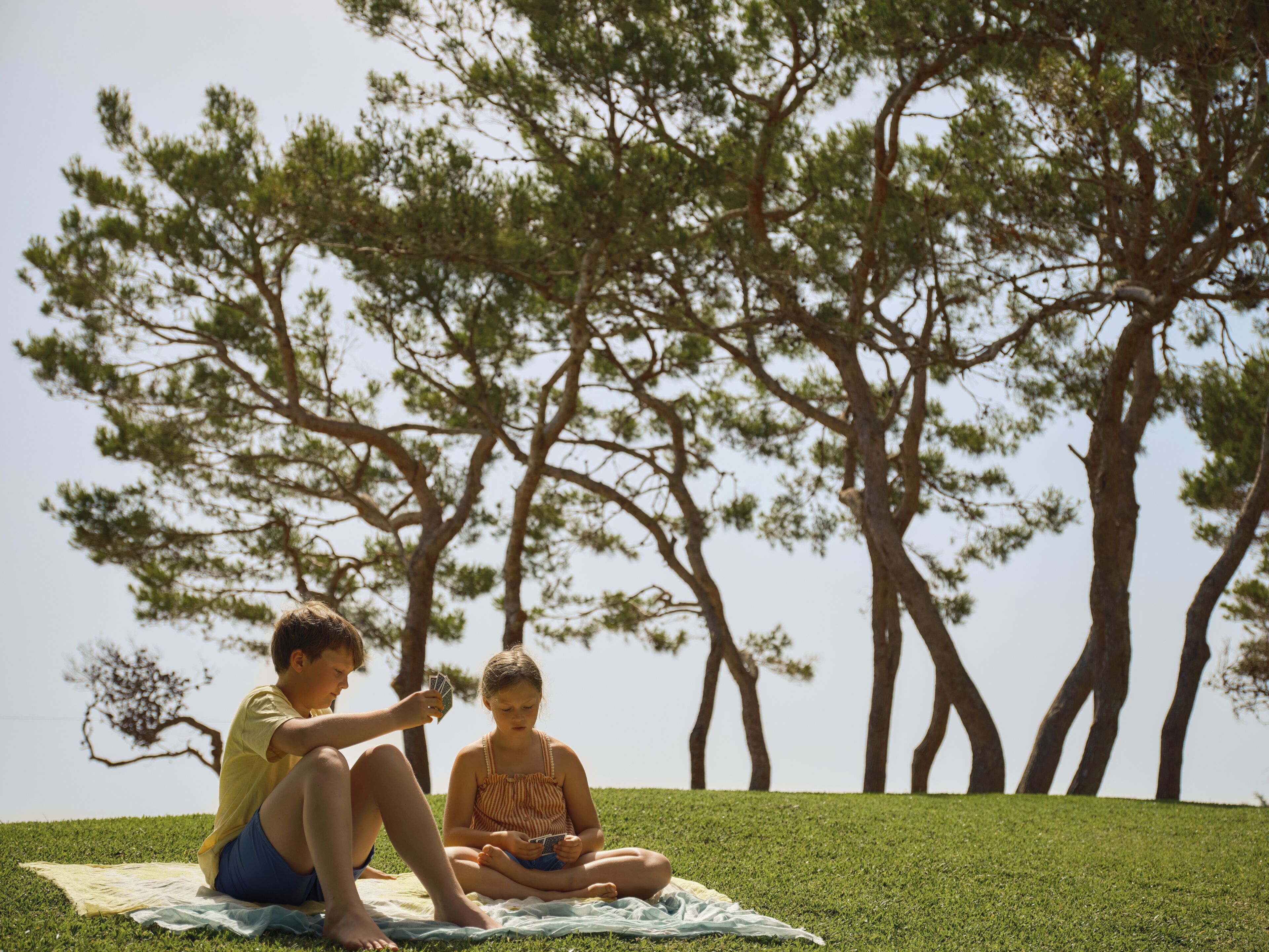 Two people sitting on a blanket on grass with trees in the background.