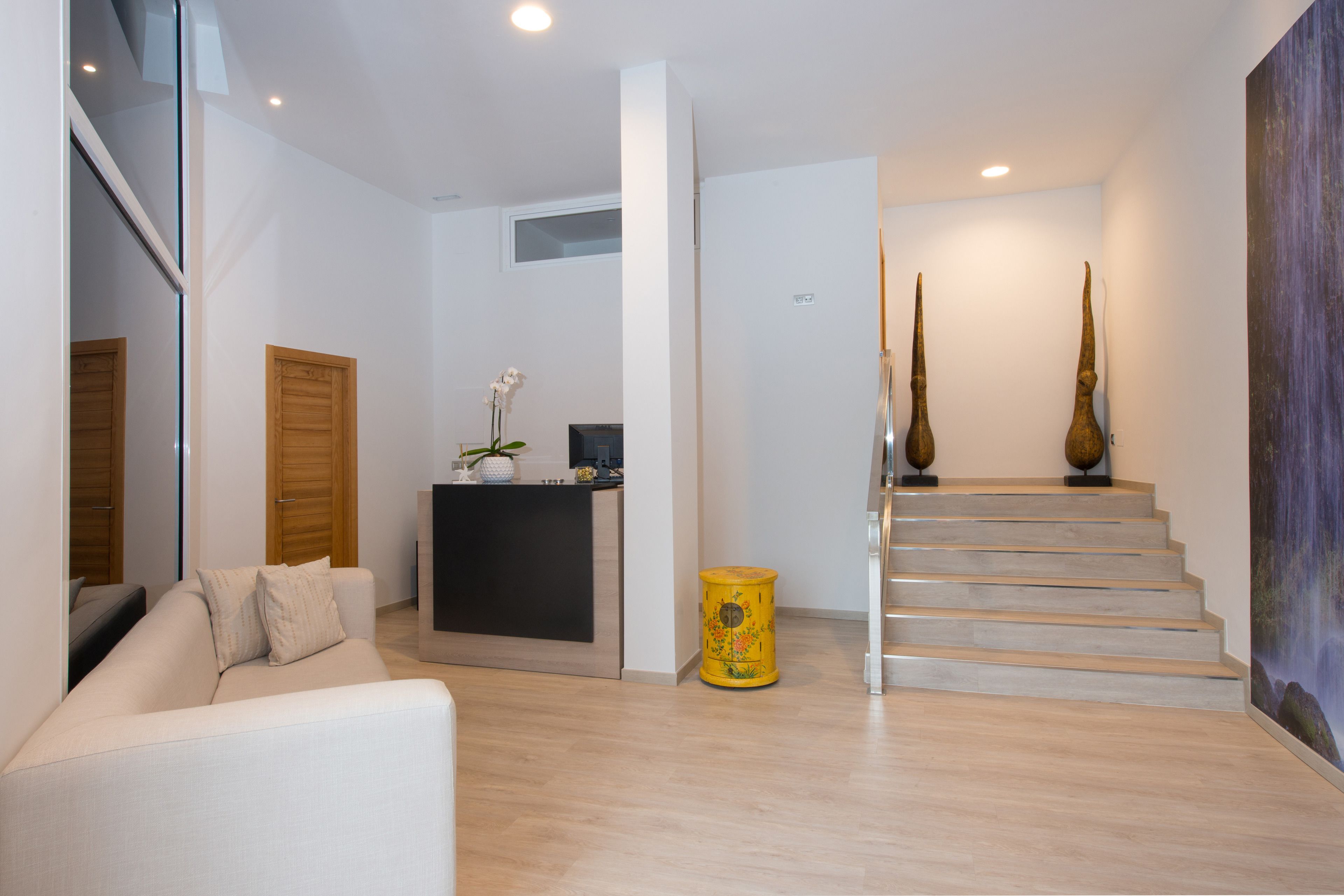 Una sala de estar moderna con un sofá, una mesita con un florero, una puerta de madera y una escalera que conduce a otro nivel.
