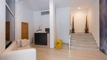 Una sala de estar moderna con un sofá, una mesita con un florero, una puerta de madera y una escalera que conduce a otro nivel.