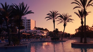 A resort pool area with palm trees, lounge chairs, and a building in the background. - Hotel Exagon Park (Santa Margalida)