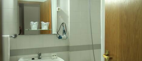 Un baño con lavamanos, espejo, ducha y puerta de madera.