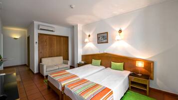 Una camera d'albergo con due letti, una testiera in legno, un tappeto verde e un comodino con una lampada.
