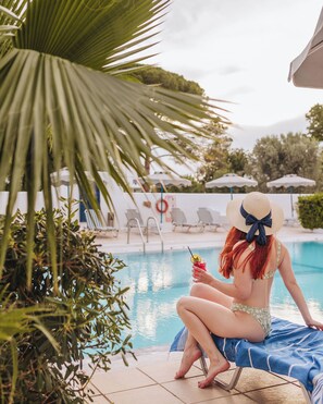 Una piscina al aire libre, sombrillas, sillones reclinables de piscina