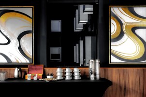 A bar area with a coffee machine, stacked white cups, and a framed abstract painting on the wall.