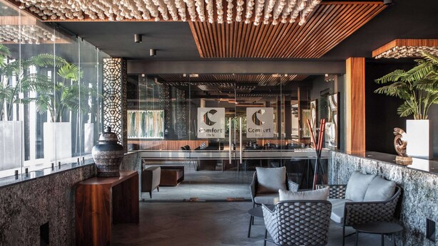 Un hall d’hôtel moderne avec une cloison en verre, un espace salon et un comptoir d’accueil.