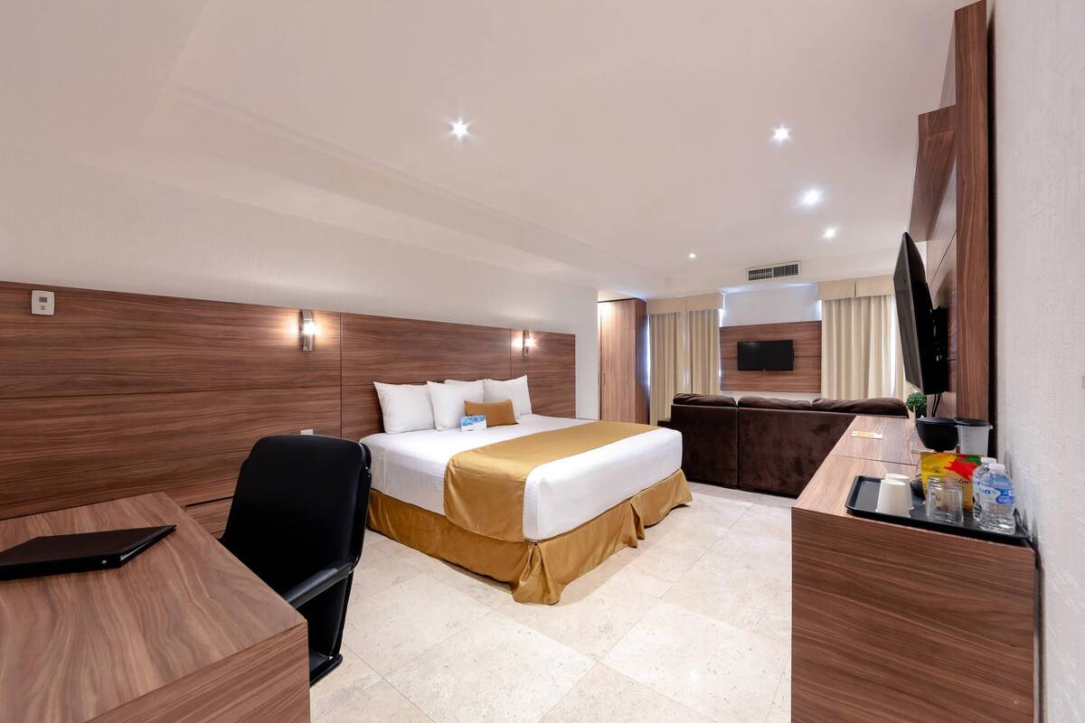 A hotel room with a bed, a desk, a chair, a TV, and a bathroom area.