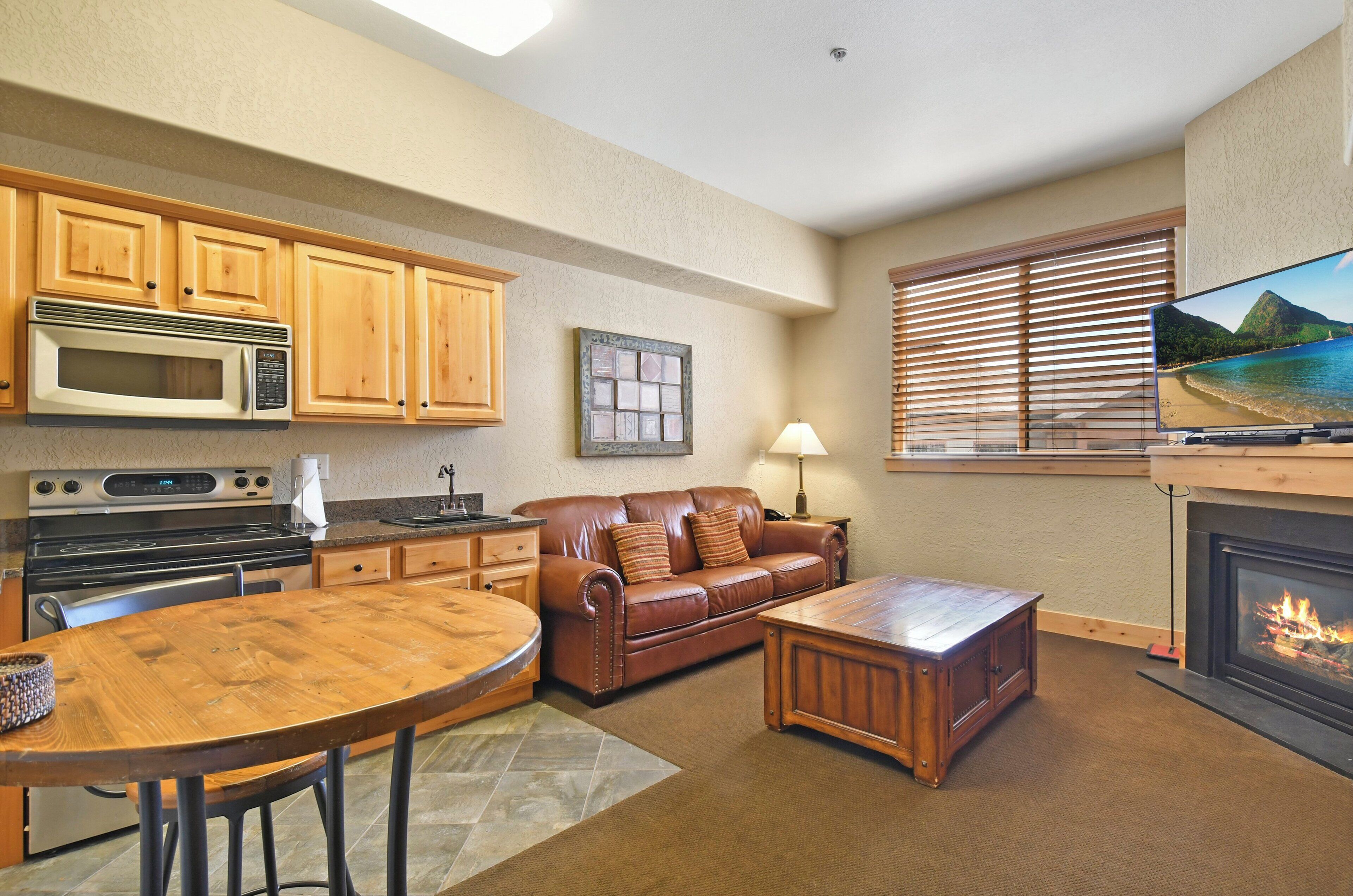A kitchen with wooden cabinets, a microwave, stove, and a dining area with a table and chairs.