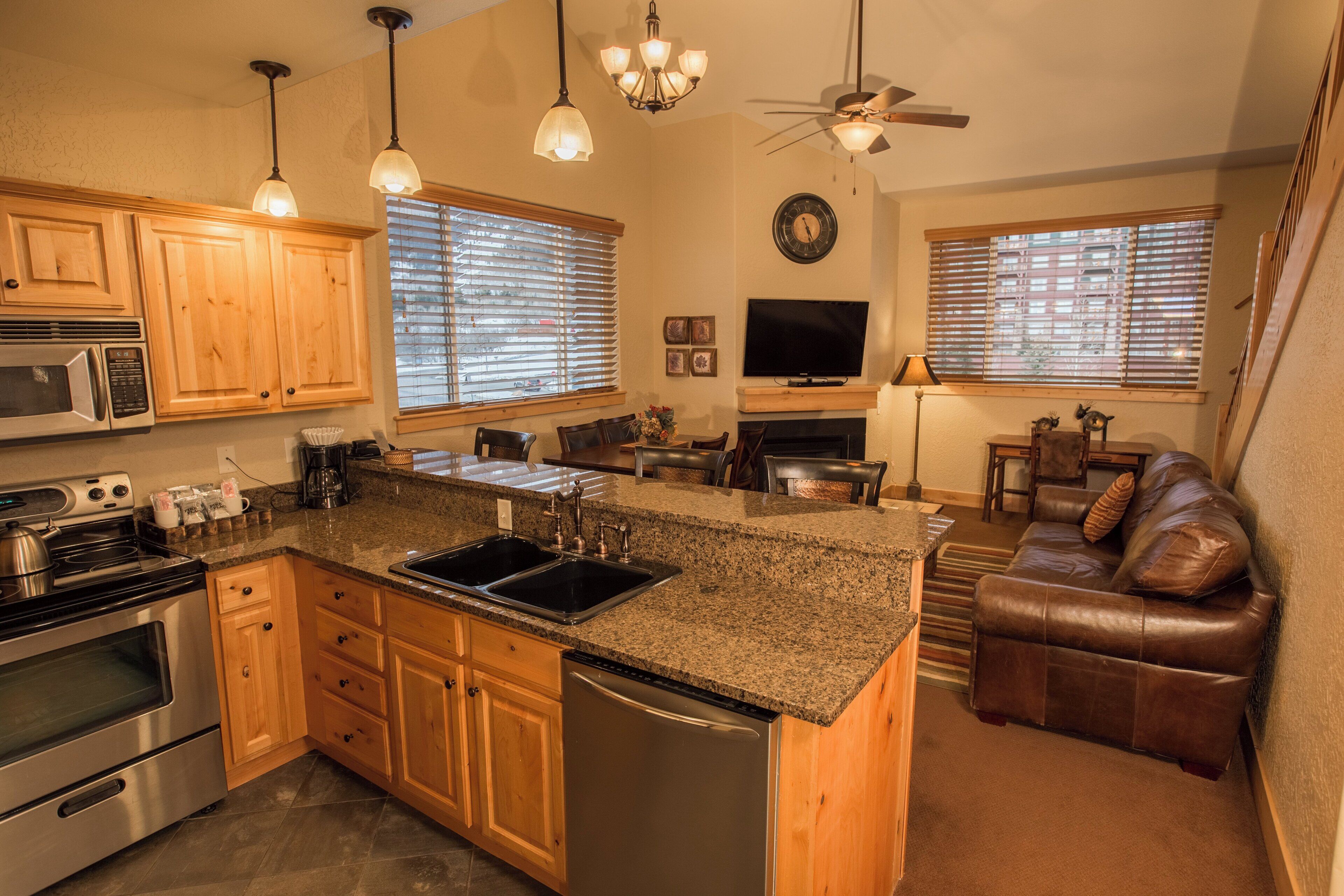 A modern kitchen with granite countertops, wooden cabinets, stainless steel appliances, and a built-in island with a sink.