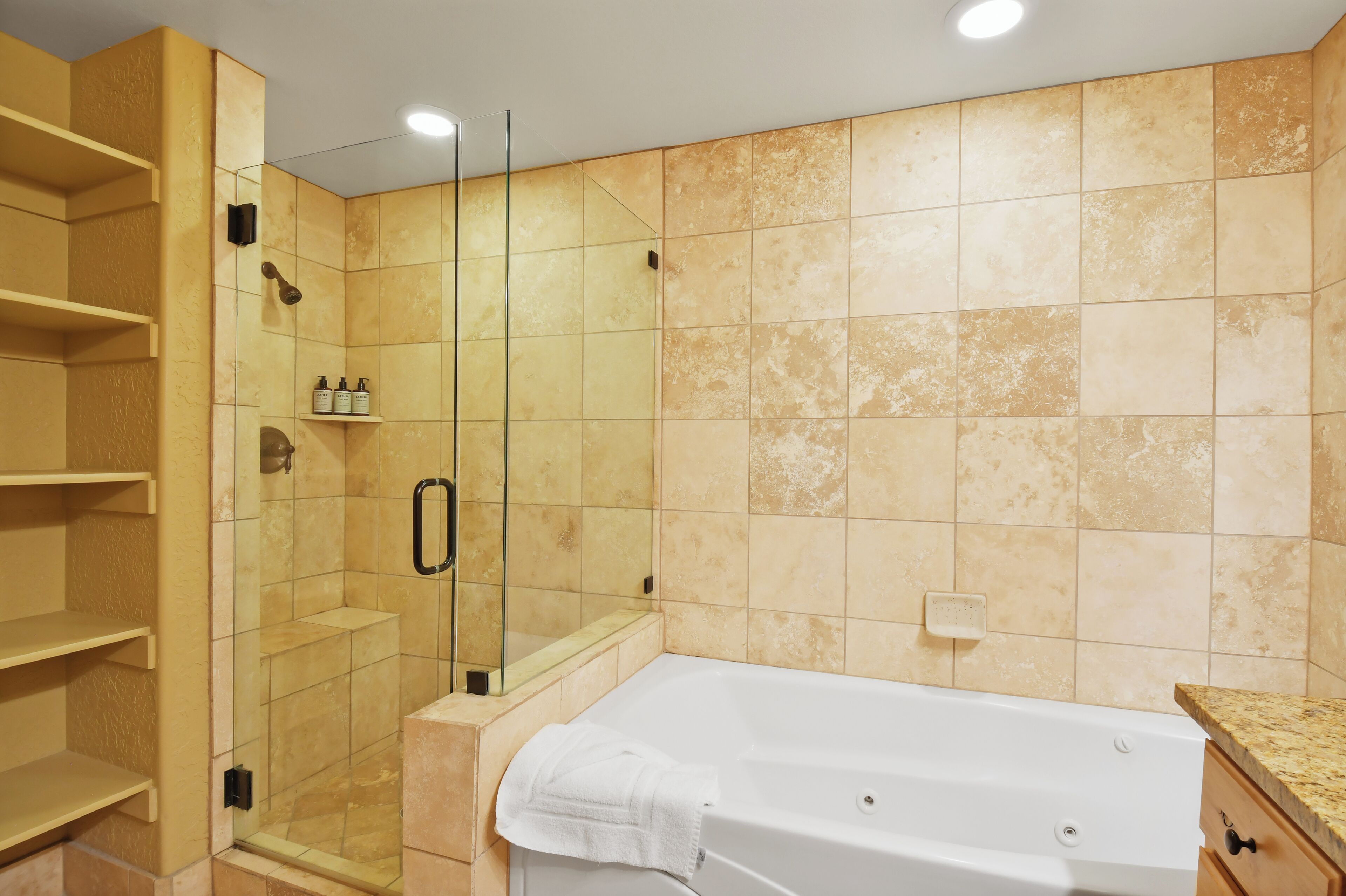 A bathroom with a glass-enclosed shower, a white bathtub, and beige tiled walls.