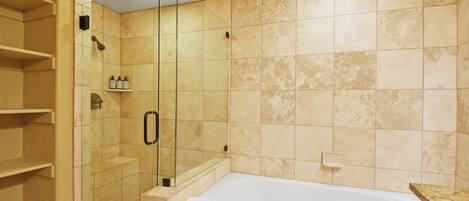 A bathroom with a glass-enclosed shower, a white bathtub, and beige tiled walls.