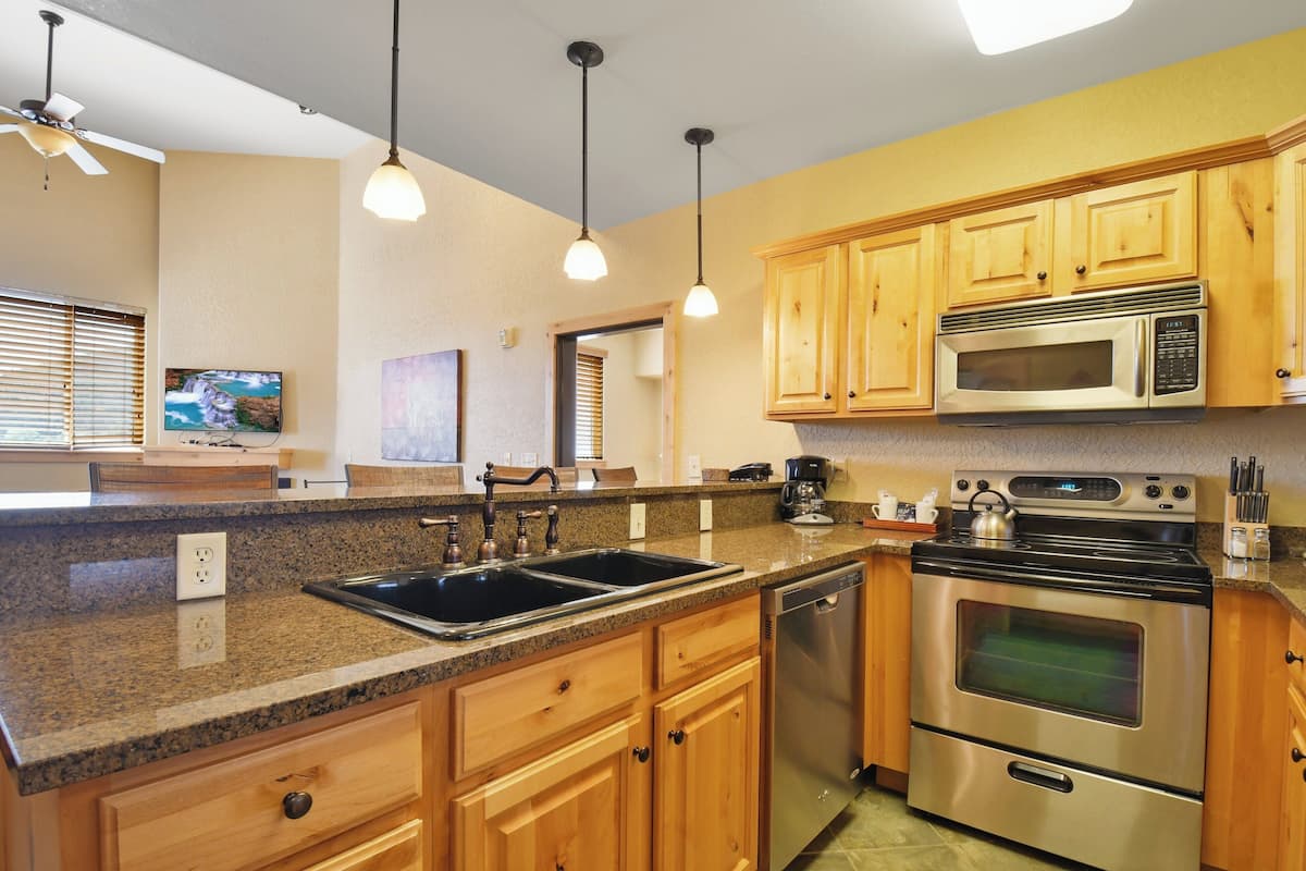 A kitchen with granite countertops, stainless steel appliances, wooden cabinets, and pendant lighting.