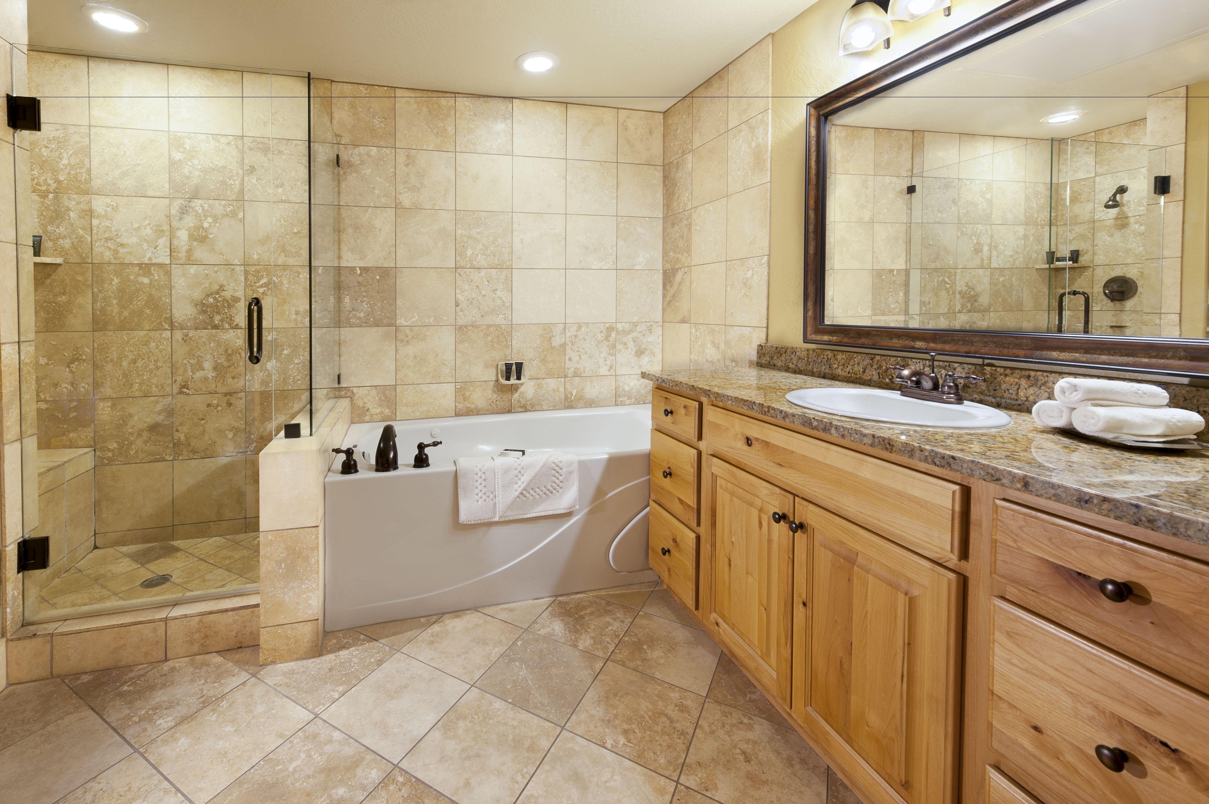 A modern bathroom with a walk-in shower, a freestanding bathtub, wooden cabinets, and a large mirror.