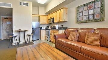 A kitchen with wooden cabinets, a microwave, and a refrigerator. There is a brown leather sofa with pillows and a wooden coffee table.