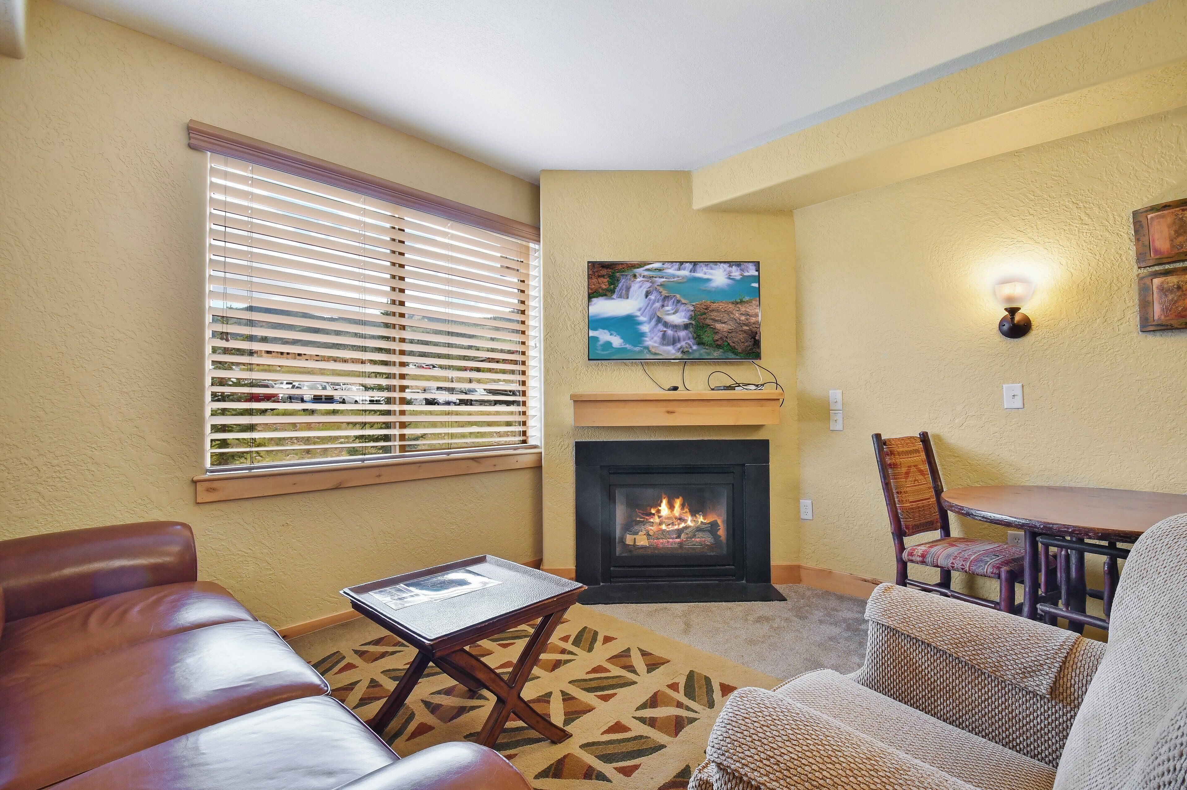 A cozy living room with a fireplace, comfortable seating, and a television mounted above it.