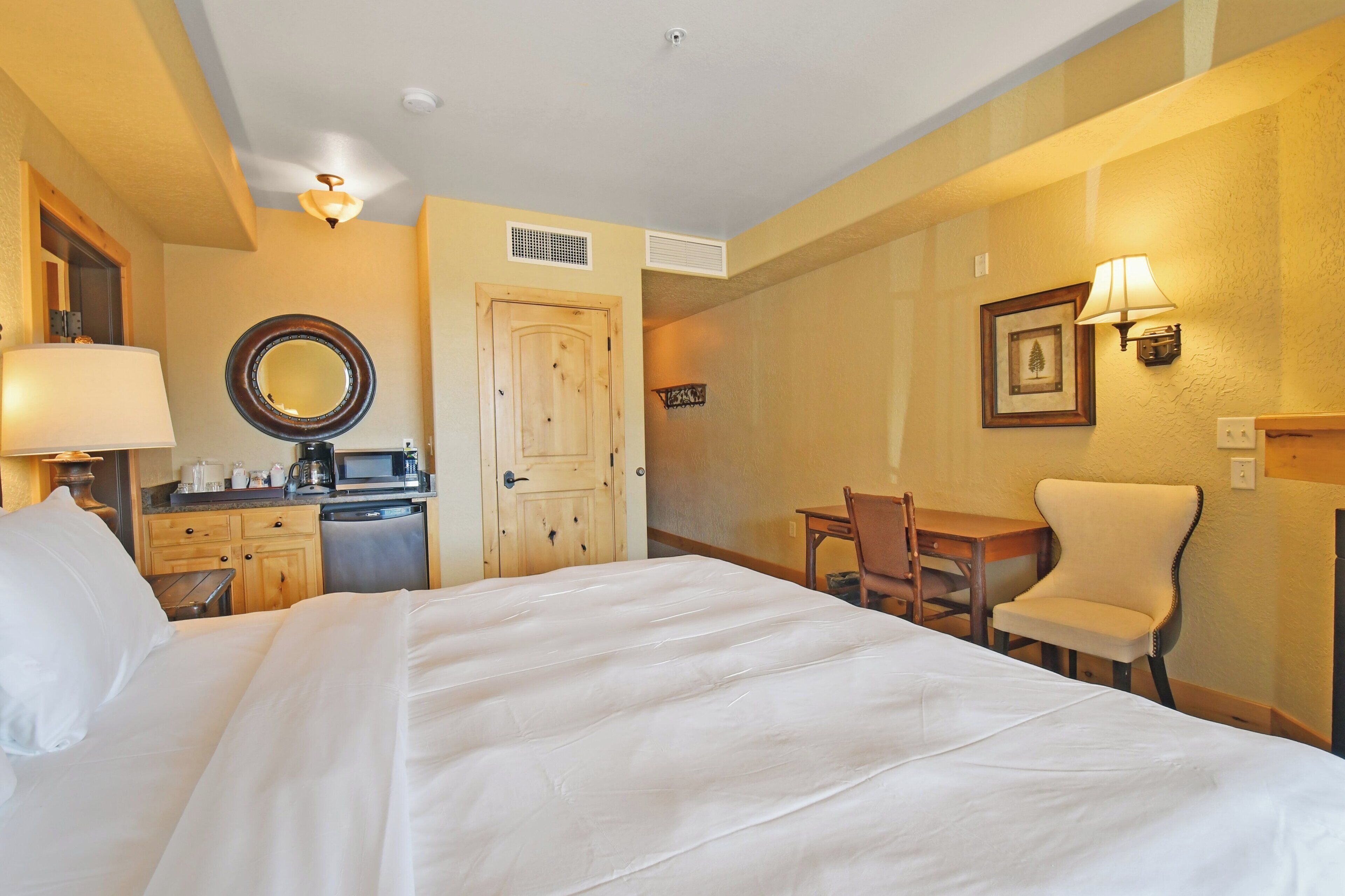 Quarto de hotel com cama, escrivaninha, cadeira, micro-ondas e cafeteira.