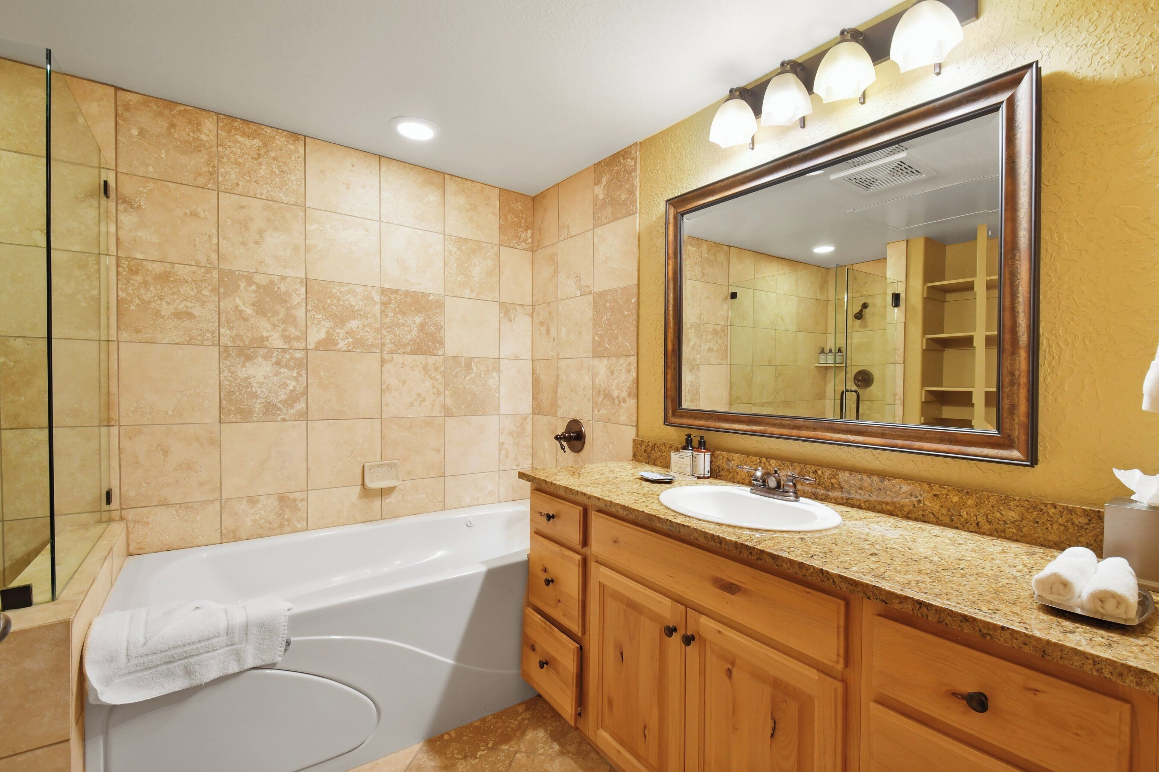A bathroom with a bathtub, a sink, wooden cabinets, a large mirror, and a towel rack.