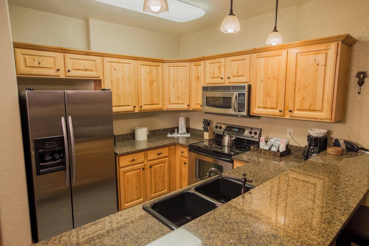 A kitchen with wooden cabinets, stainless steel appliances, granite countertops, and pendant lighting.