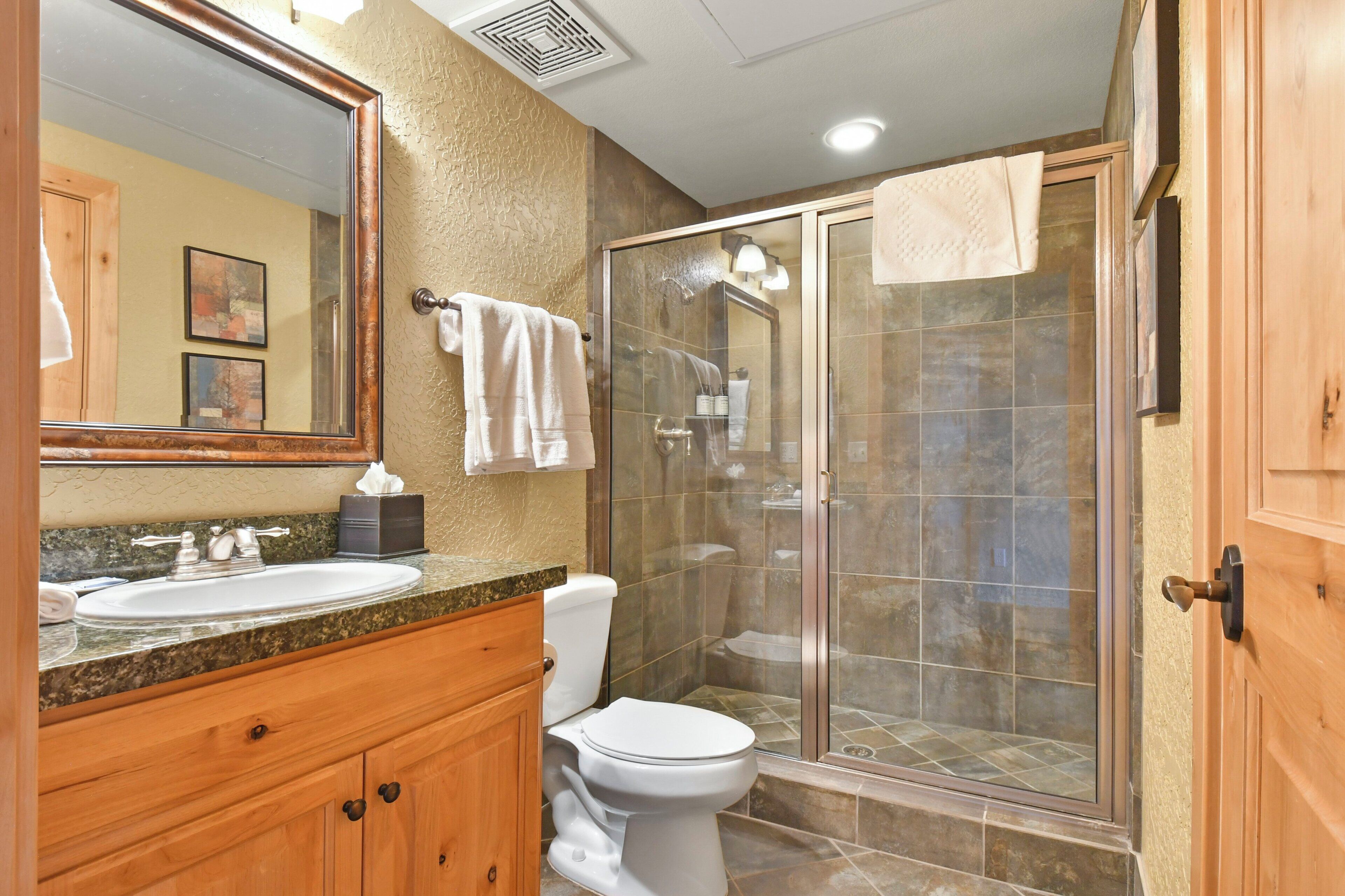 Une salle de bain équipée d’un lavabo, de toilettes et d’une douche fermée par des parois en verre.