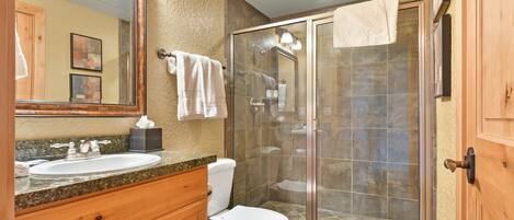 Une salle de bain équipée d’un lavabo, de toilettes et d’une douche fermée par des parois en verre.