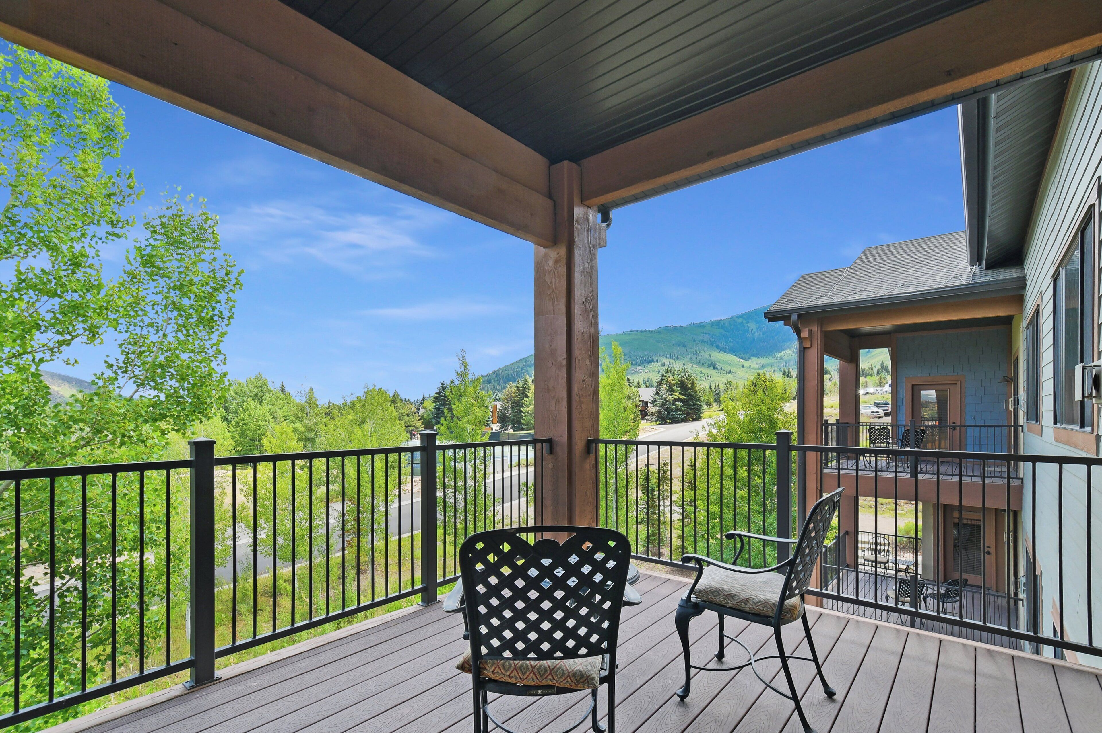 A wooden deck with two chairs, a railing, and a view of a mountain and greenery.
