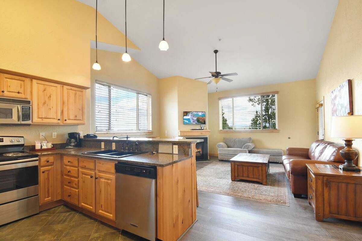 A kitchen with wooden cabinets, a dishwasher, and a microwave. There is a dining area with a sofa and a coffee table.