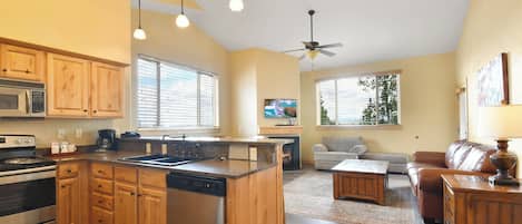 A kitchen with wooden cabinets, a dishwasher, and a microwave. There is a dining area with a sofa and a coffee table.