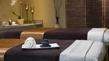 A spa room with two massage beds, a towel, a stone, and a small plant.