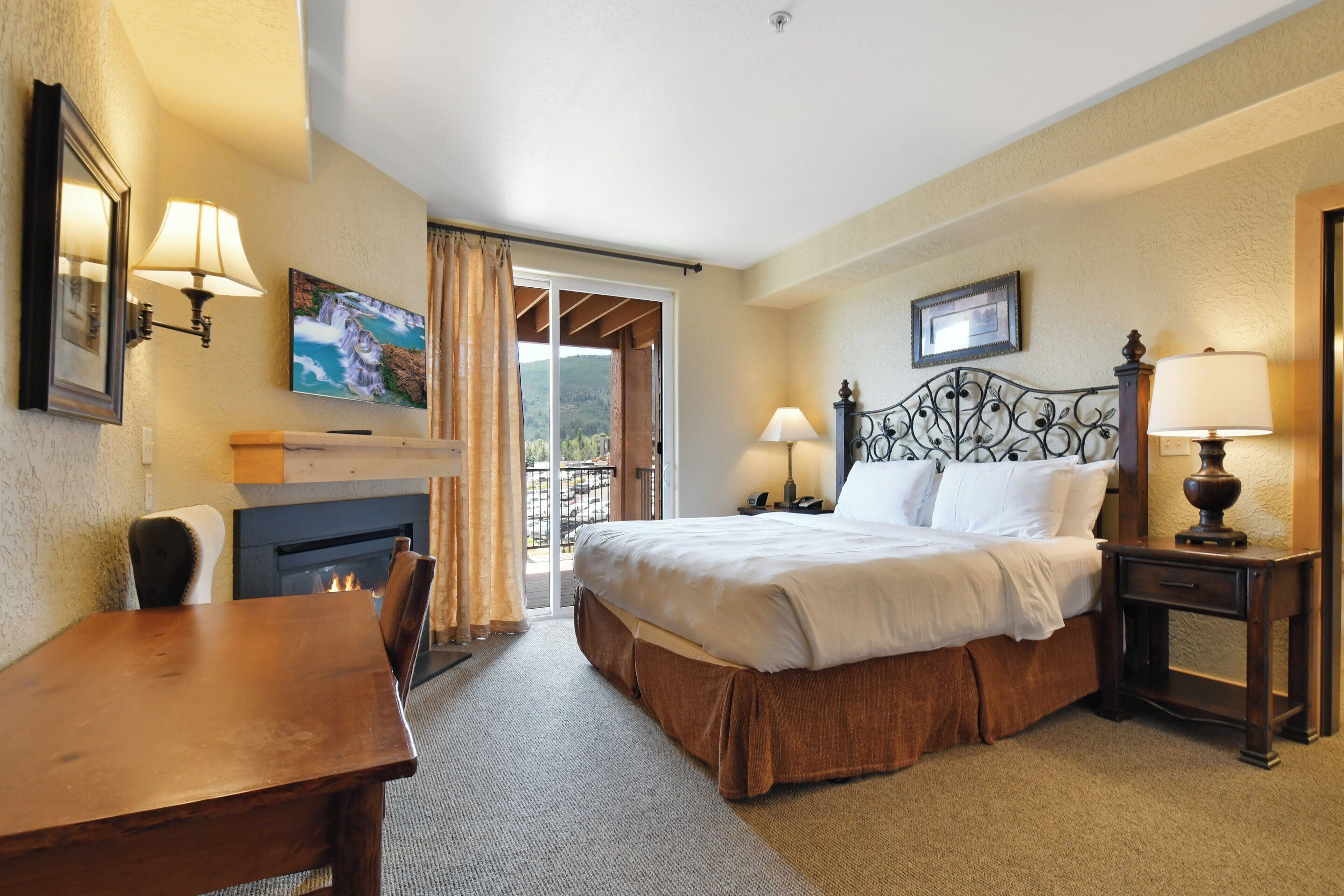 Quarto de hotel com cama, escrivaninha, lareira e varanda com vista.
