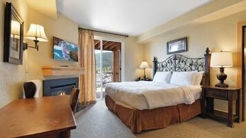 Quarto de hotel com cama, escrivaninha, lareira e varanda com vista.