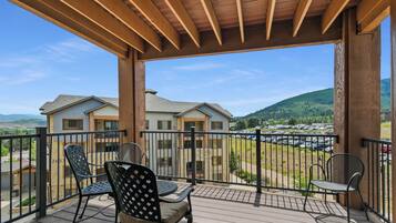 A balcony with two chairs and a table, overlooking a parking lot and houses.