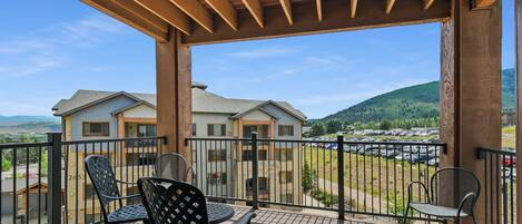 A balcony with two chairs and a table, overlooking a parking lot and houses.