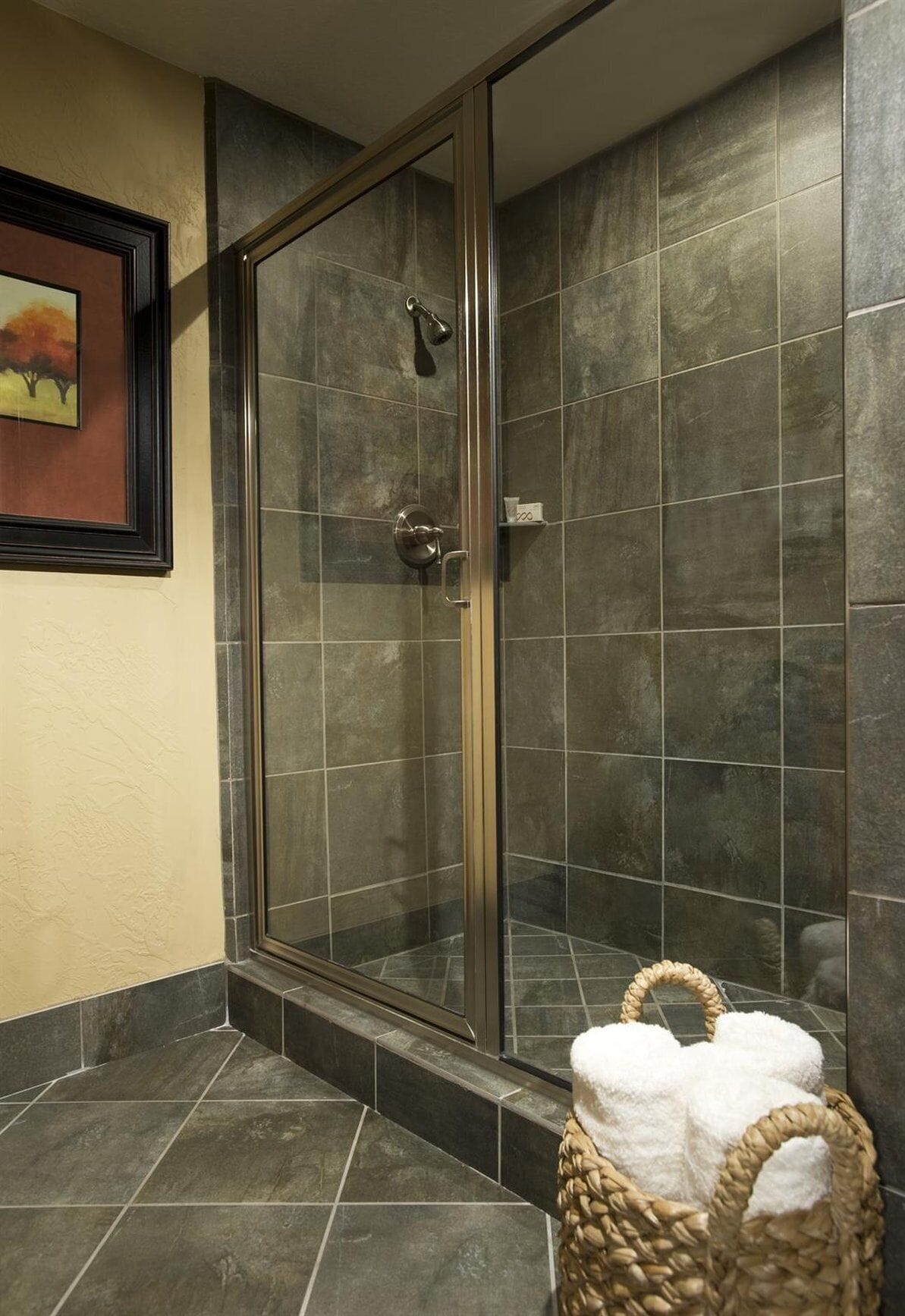 Eine Dusche mit Glastür, gefliesten Wänden und einem Korb mit Handtüchern.
