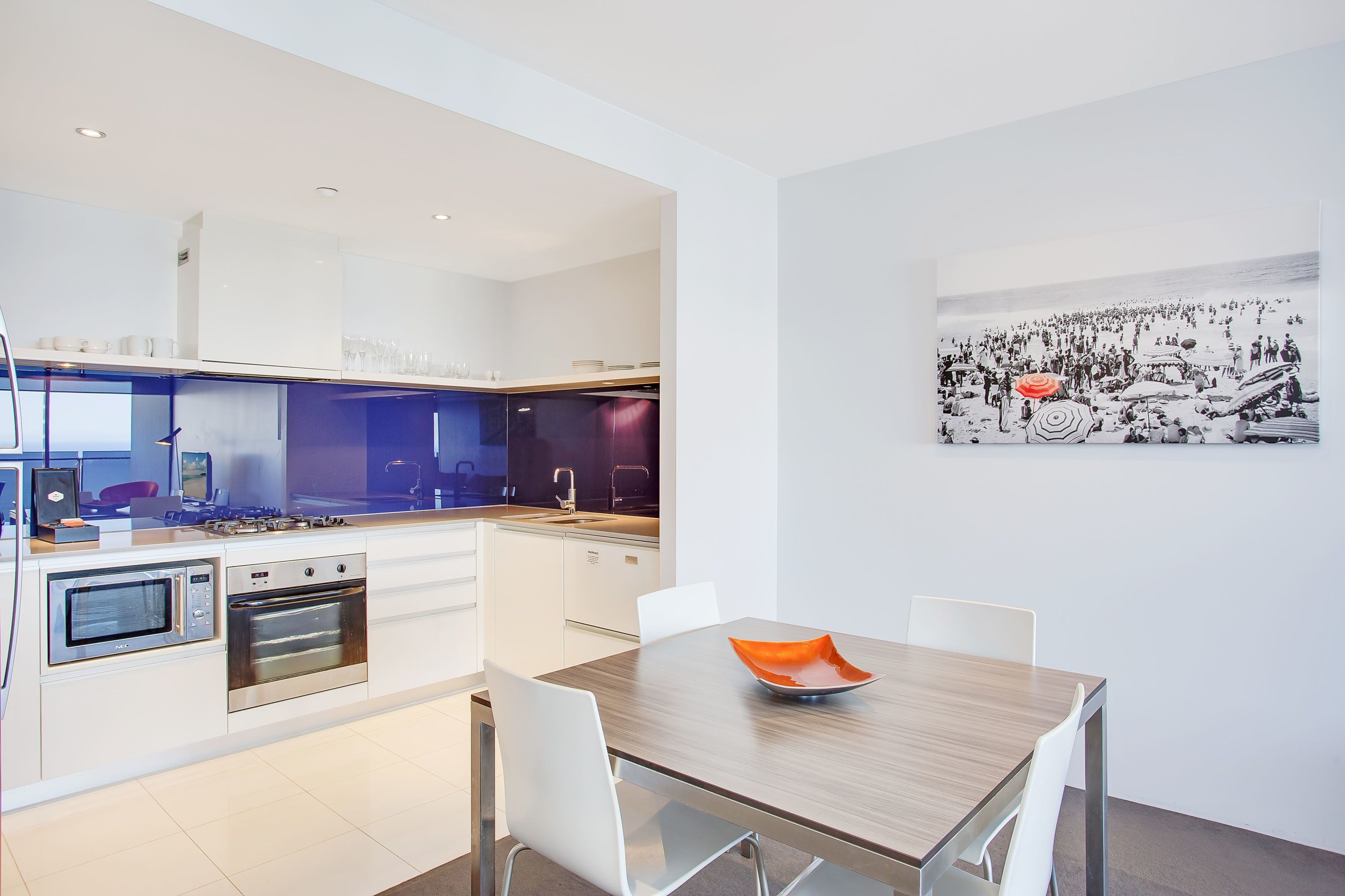 A modern kitchen with white cabinets, stainless steel appliances, and a dining area with a wooden table and white chairs.