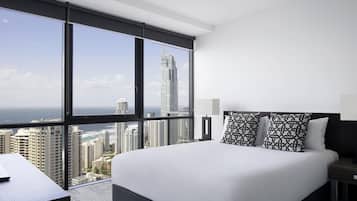 Habitación de hotel moderna con una cama grande, un escritorio y vistas a un horizonte urbano y al océano.