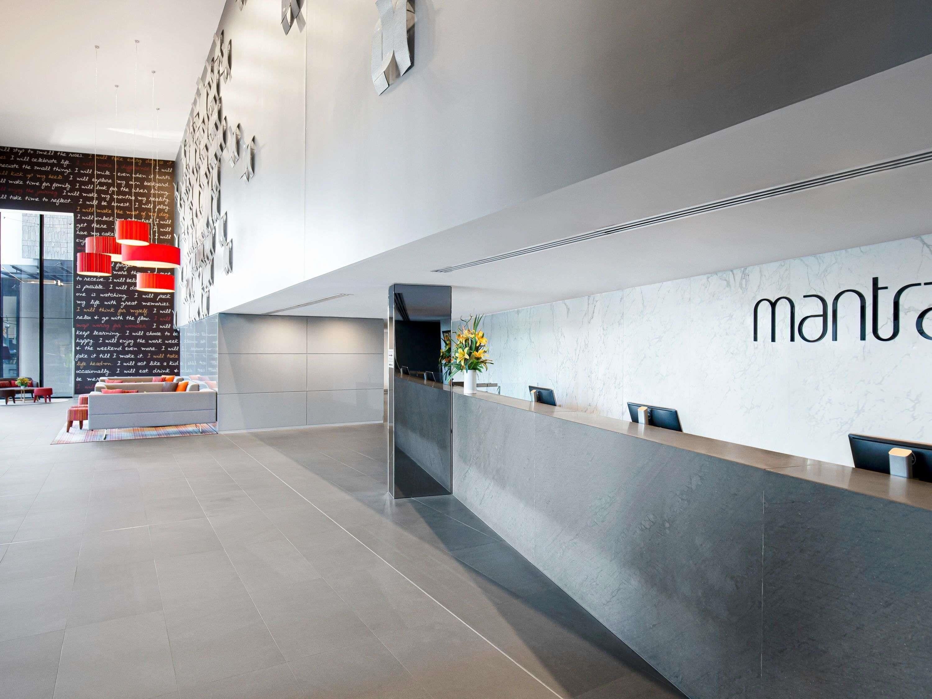 A modern reception area with a marble wall, a reception desk, and a seating area with a red accent wall.