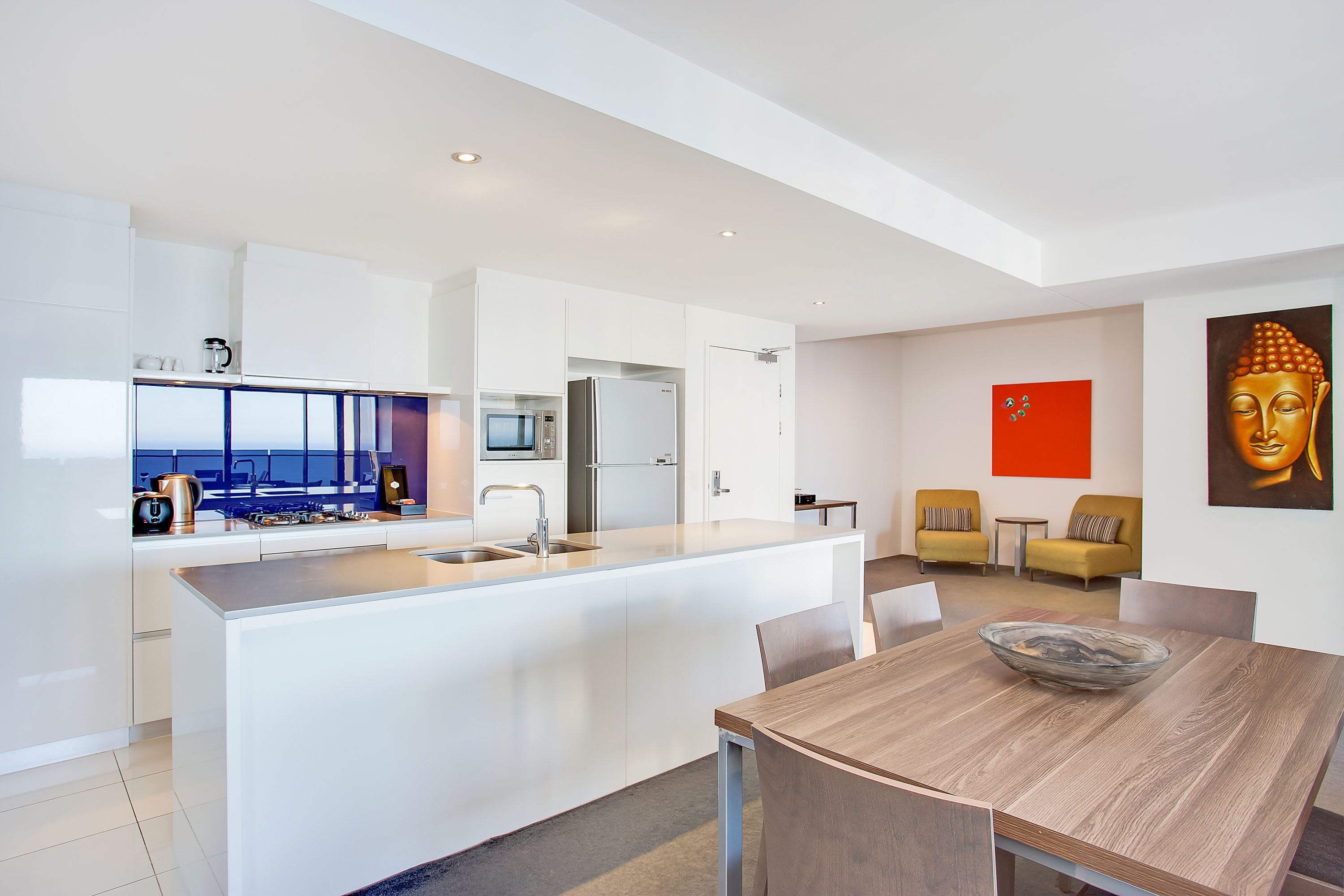 A modern kitchen with white cabinetry, a central island, and a dining area with a wooden table and chairs.