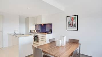 A modern kitchen with white cabinetry, a wooden dining table with chairs, and a framed picture on the wall.