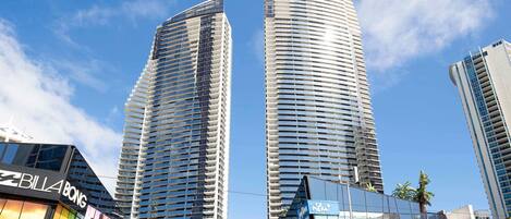 Two high-rise buildings with reflective glass facades, a modern shopping center with a curved roof, and a visible sign for 'Billa BONG'.