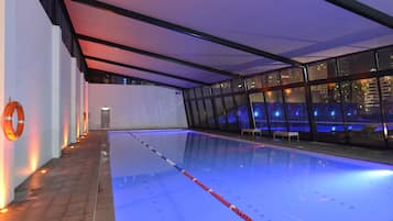 Una piscina con carriles claramente delimitados, un flotador en la pared y vistas a la ciudad a través de grandes ventanales.