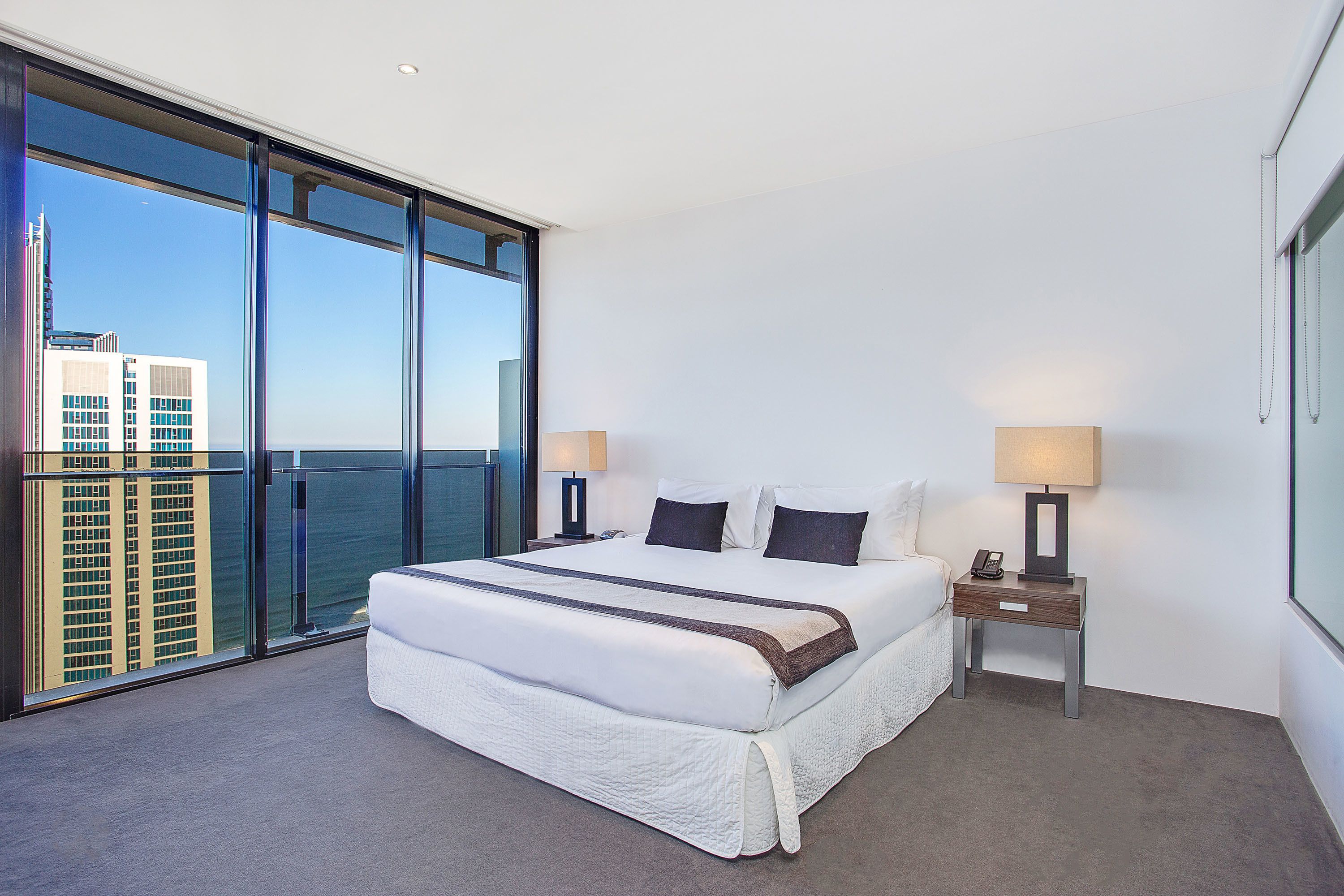 A hotel room with a large bed, two bedside tables, a view of the city, and a balcony.